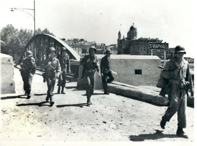 Soldiers marching on a bridge. In the back a sign saying "Saint-Raphäel"