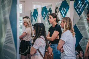 Students standing in front of the exhibition panels. They are immersed in the reading of the stories.